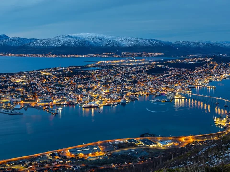 Tromsø by om kvelden sett fra Fløya – opplyste gater og snødekte fjell