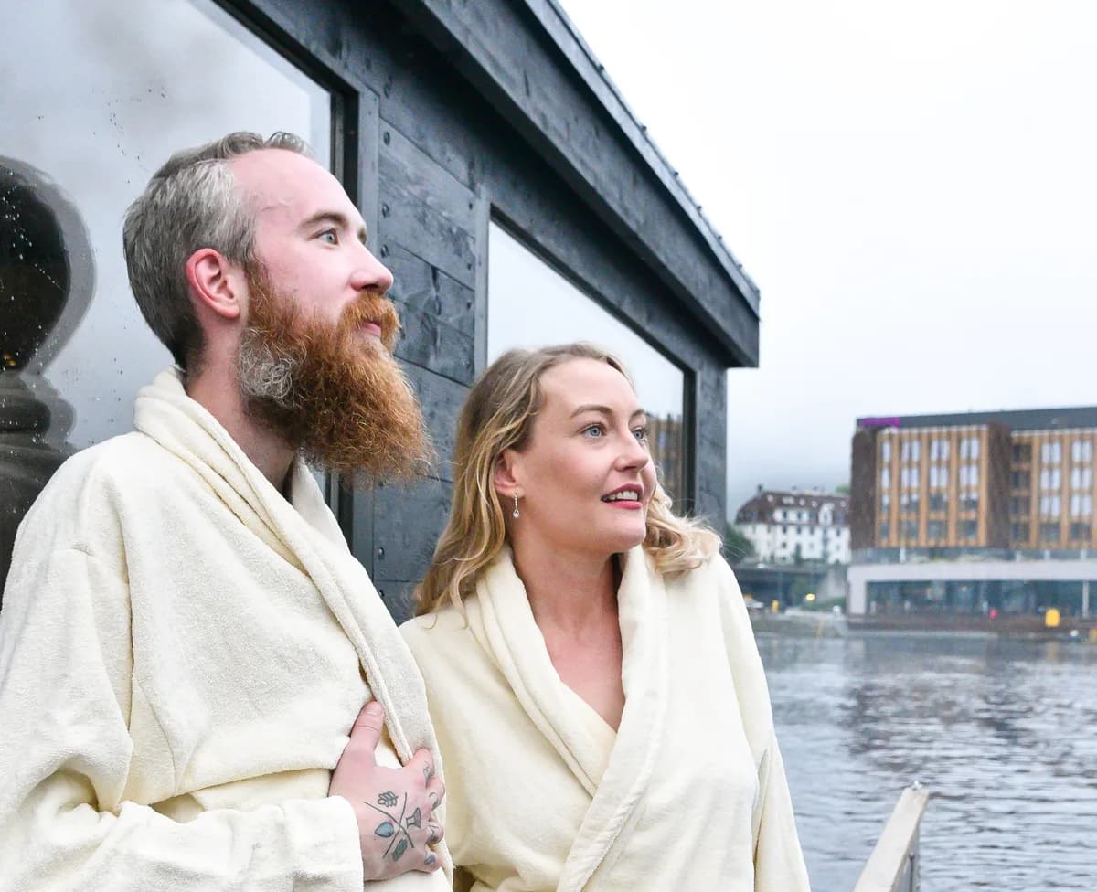 To gjester i badekåper på dekket til City Sauna Bergen med havnen i bakgrunnen