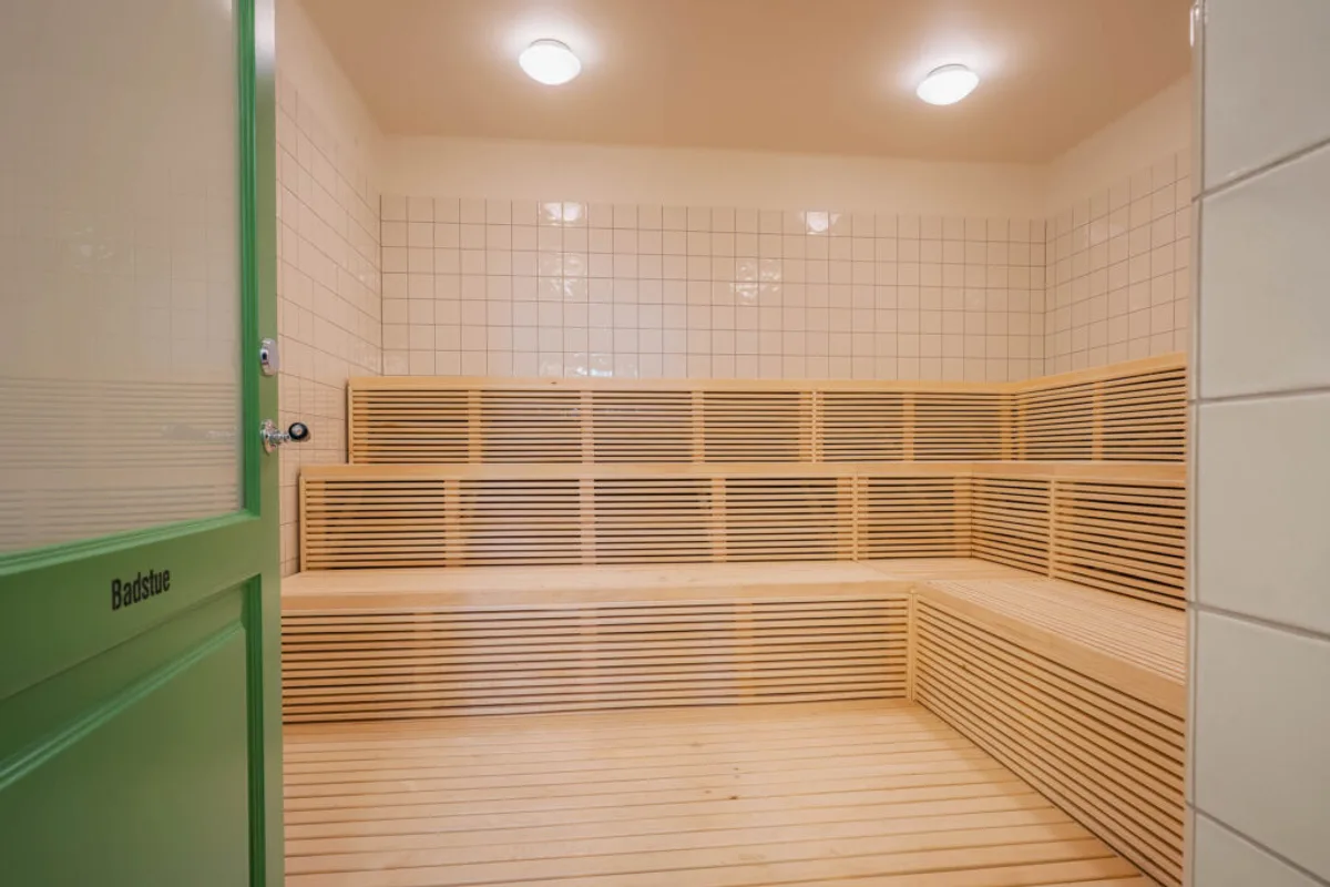 Badstue med trebenker og grønn dør inne i Sagene Folkebad i Oslo