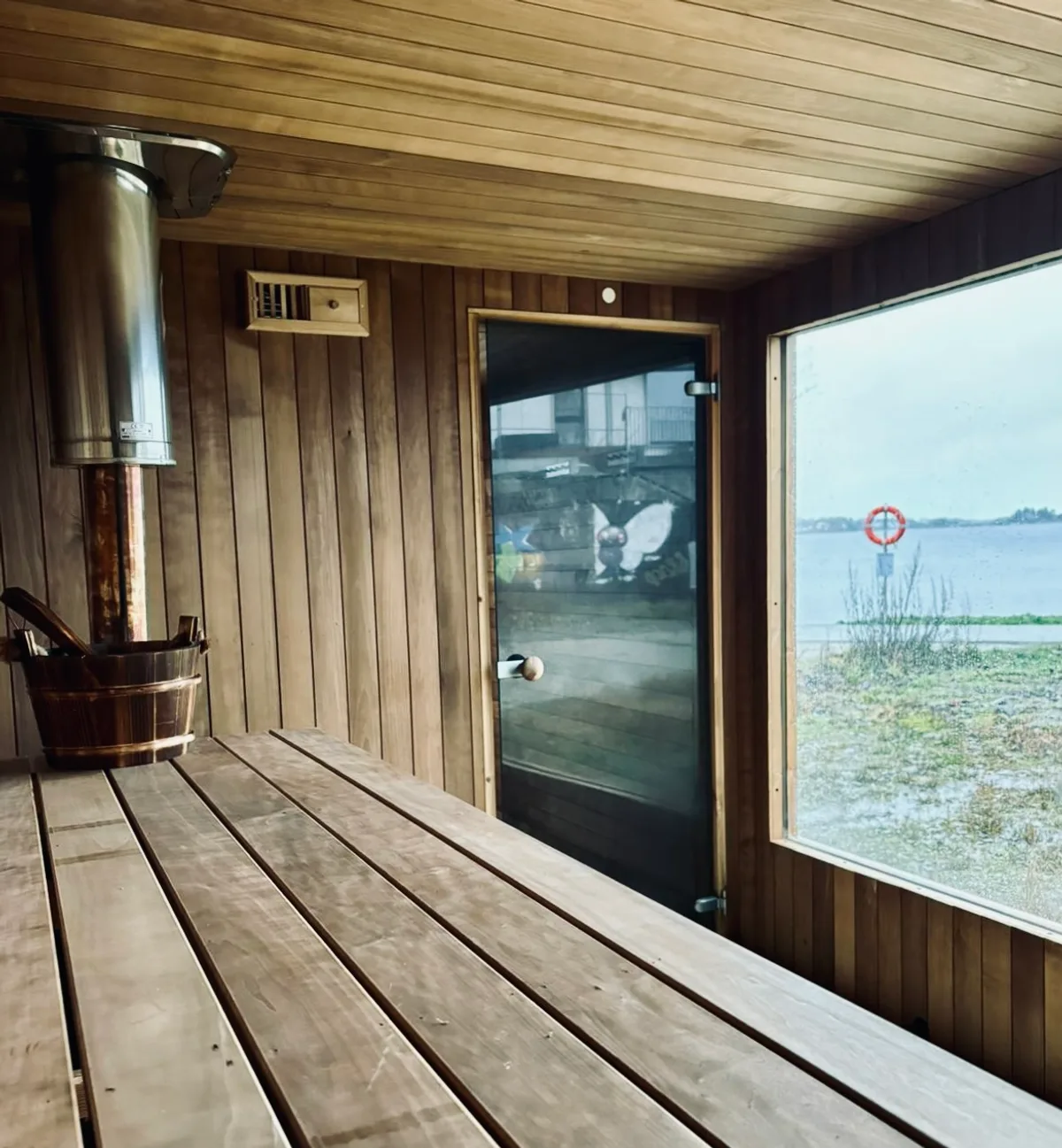 Interiør i BookSauna Sven i Stavanger med vedfyrt ovn, trebenker og sjøutsikt